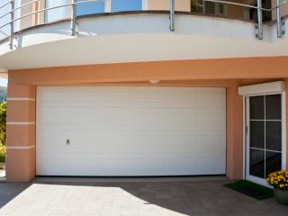 Modern White Garage Door – Fern Park Home Front view of a modern white garage door installed on a peach-colored home in Fern Park, Florida, with a potted plant by the entrance.