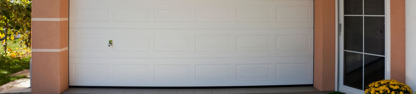Front view of a modern white garage door installed on a peach-colored home in Fern Park, Florida, with a potted plant by the entrance.