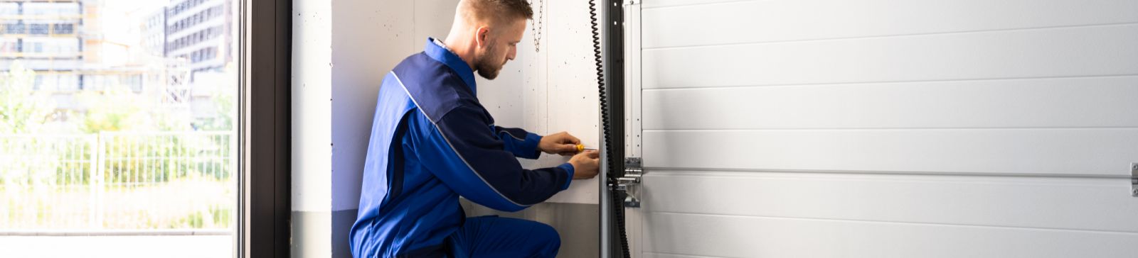 A professional technician in blue uniform kneeling inside a garage, adjusting the opener and track system with a toolbox nearby in Fern Park, FL.